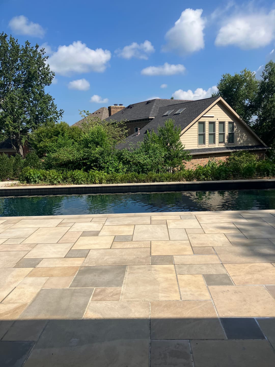 Luxury backyard with a pool, patio, and lush greenery under a blue sky.