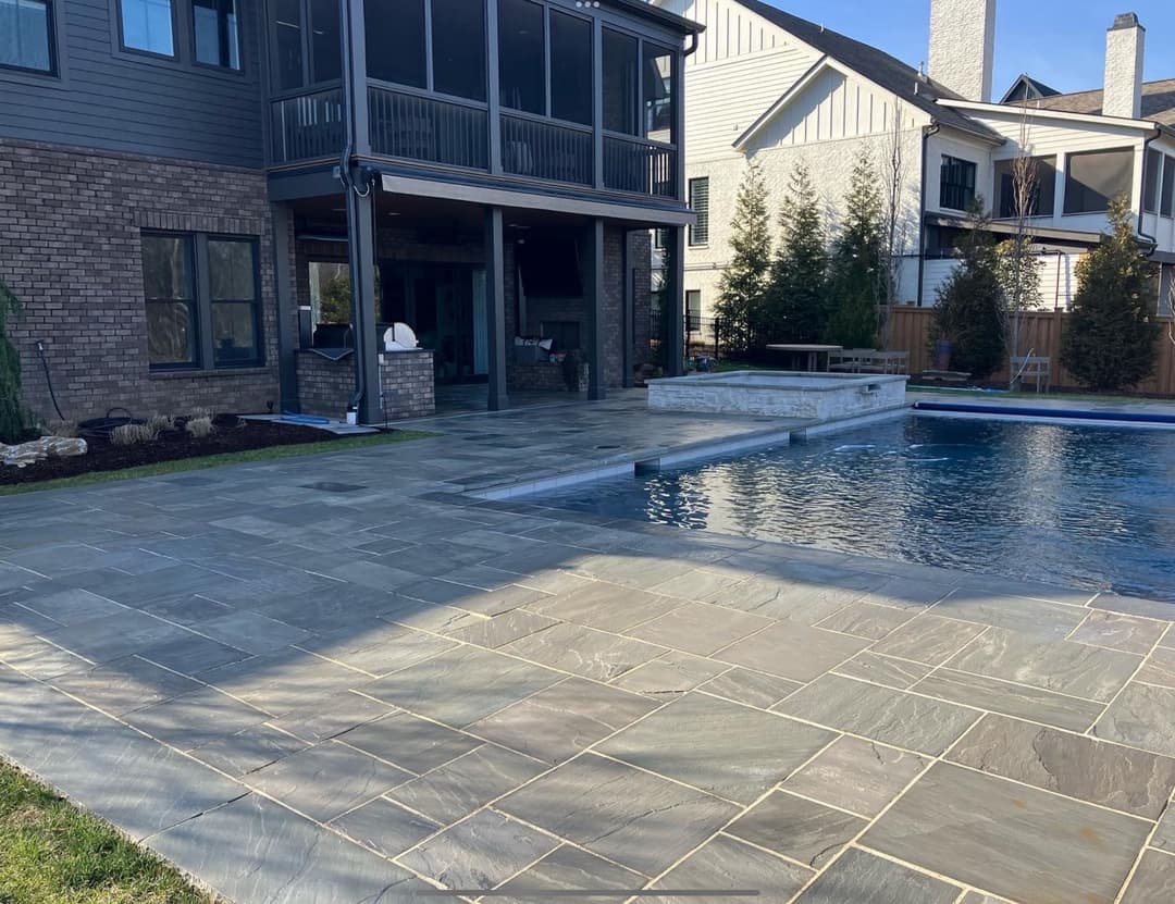 Modern backyard with a swimming pool, stone patio, and stylish home exterior.