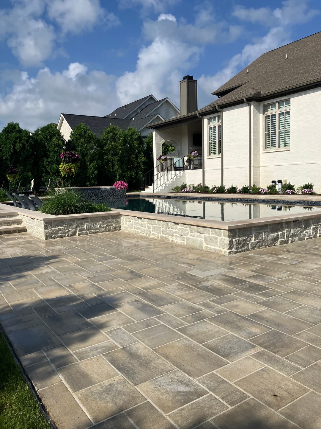 Modern backyard with stone patio, swimming pool, and lush greenery in a residential setting.