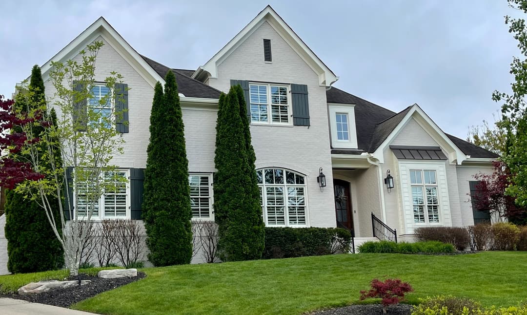 Charming two-story white brick house with dark shutters and landscaped yard.