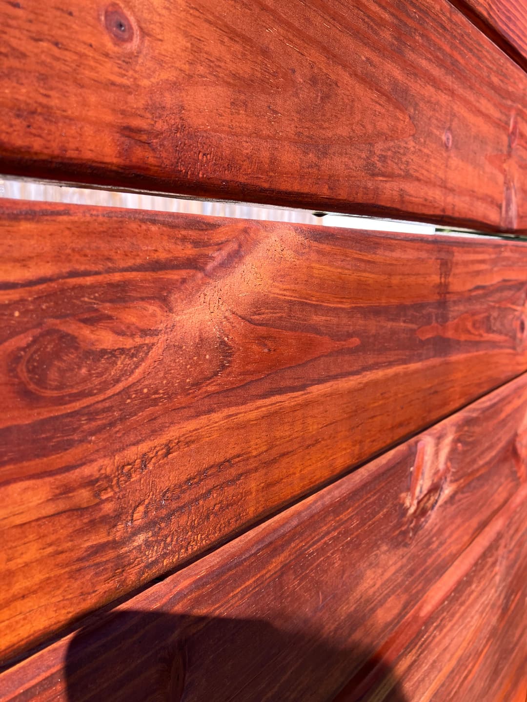 Close-up of a natural wood panel with rich reddish-brown color and visible grain texture.