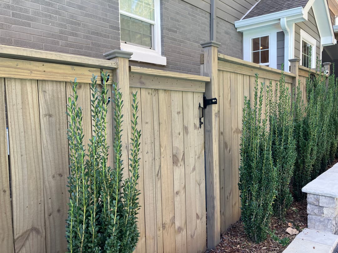 Wooden fence with gate alongside lush greenery and residential home exterior.