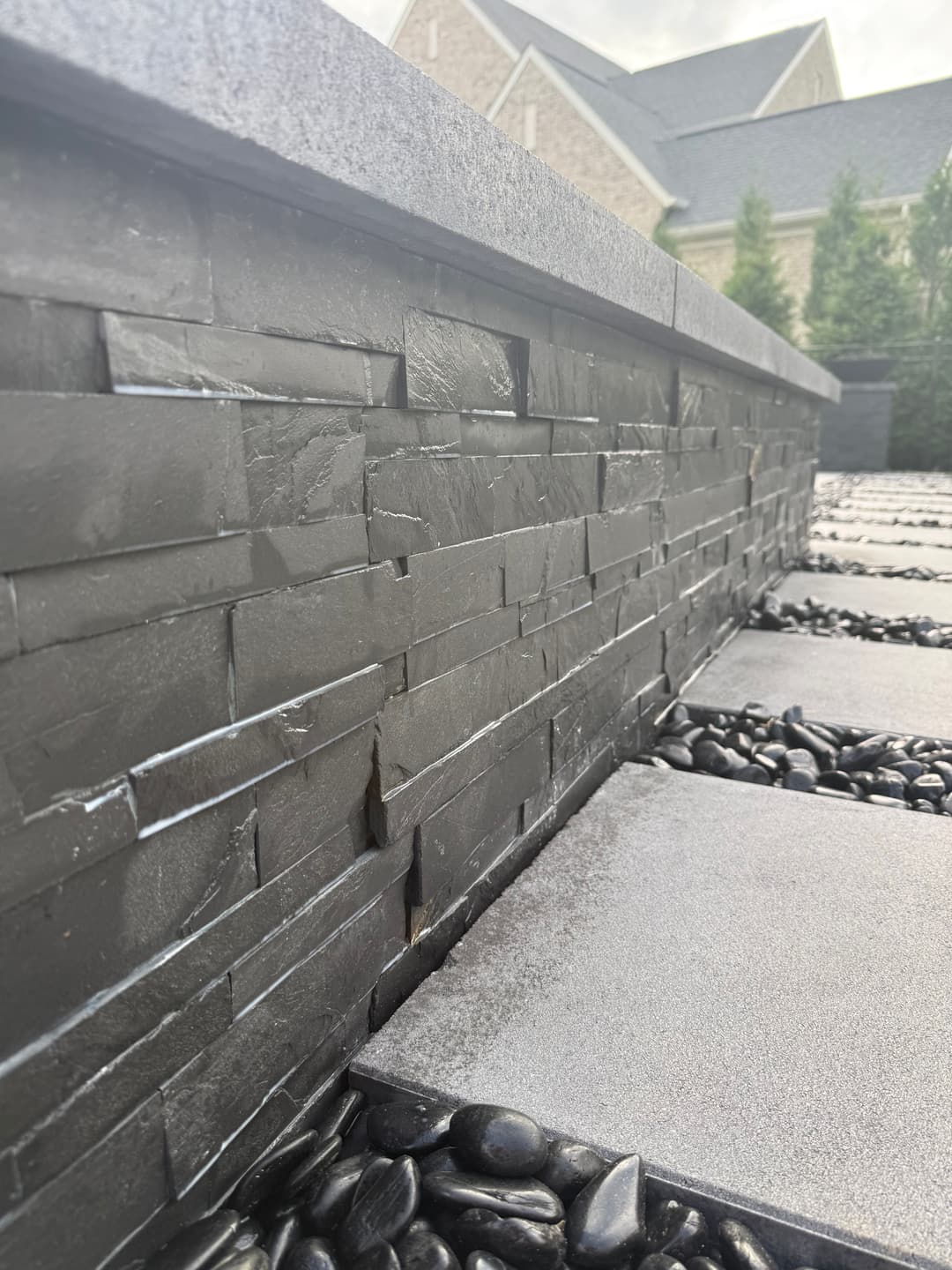 Modern stone wall with sleek black layers and pebble pathway in a landscaped outdoor space.