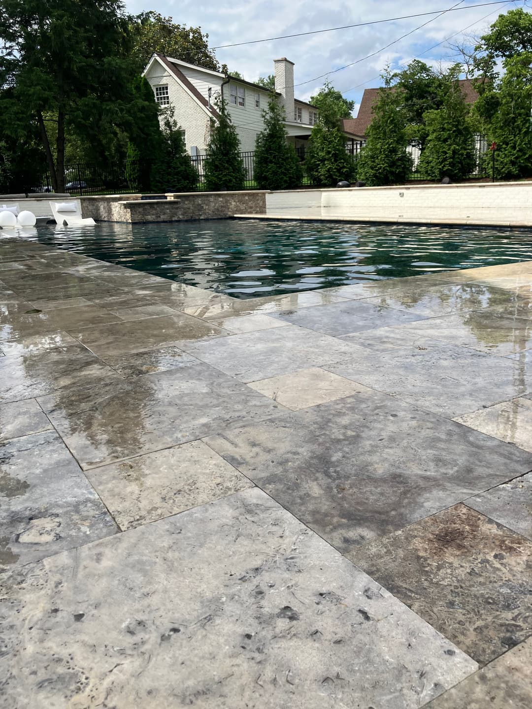 Luxury backyard pool surrounded by elegant stone tiles and lush greenery.