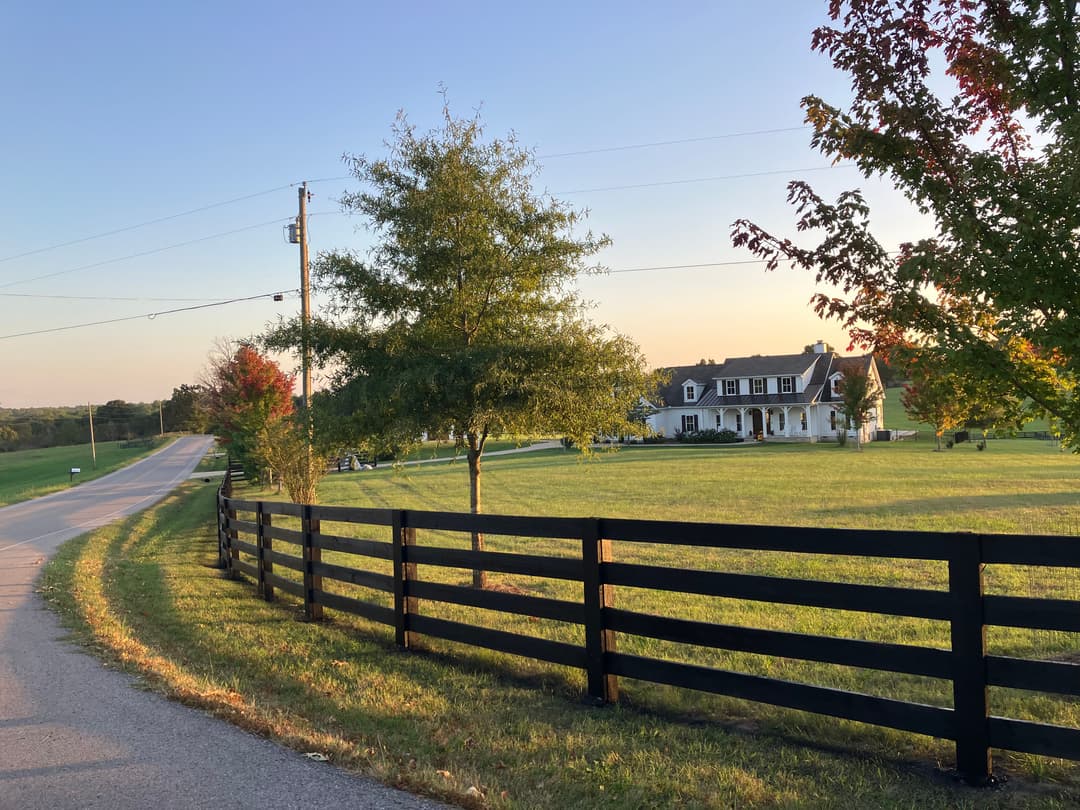 Scenic country road with a charming white farmhouse and colorful autumn trees.