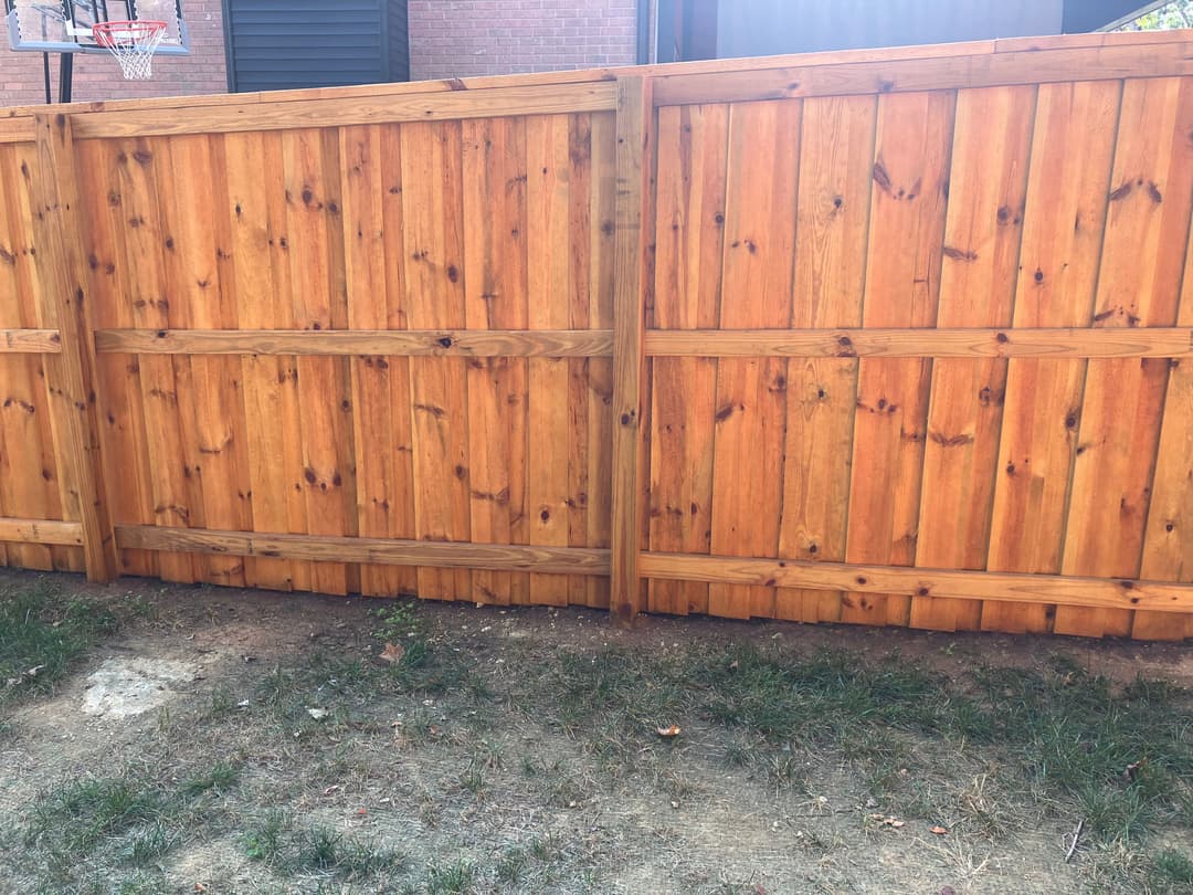 Wooden backyard fence with a basketball hoop in the background, featuring natural finish and grass area.