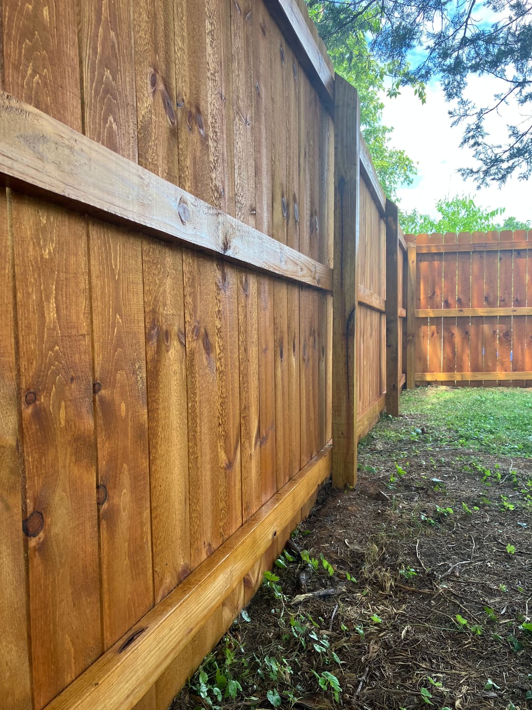 Wooden privacy fence in a garden setting with green grass and trees.