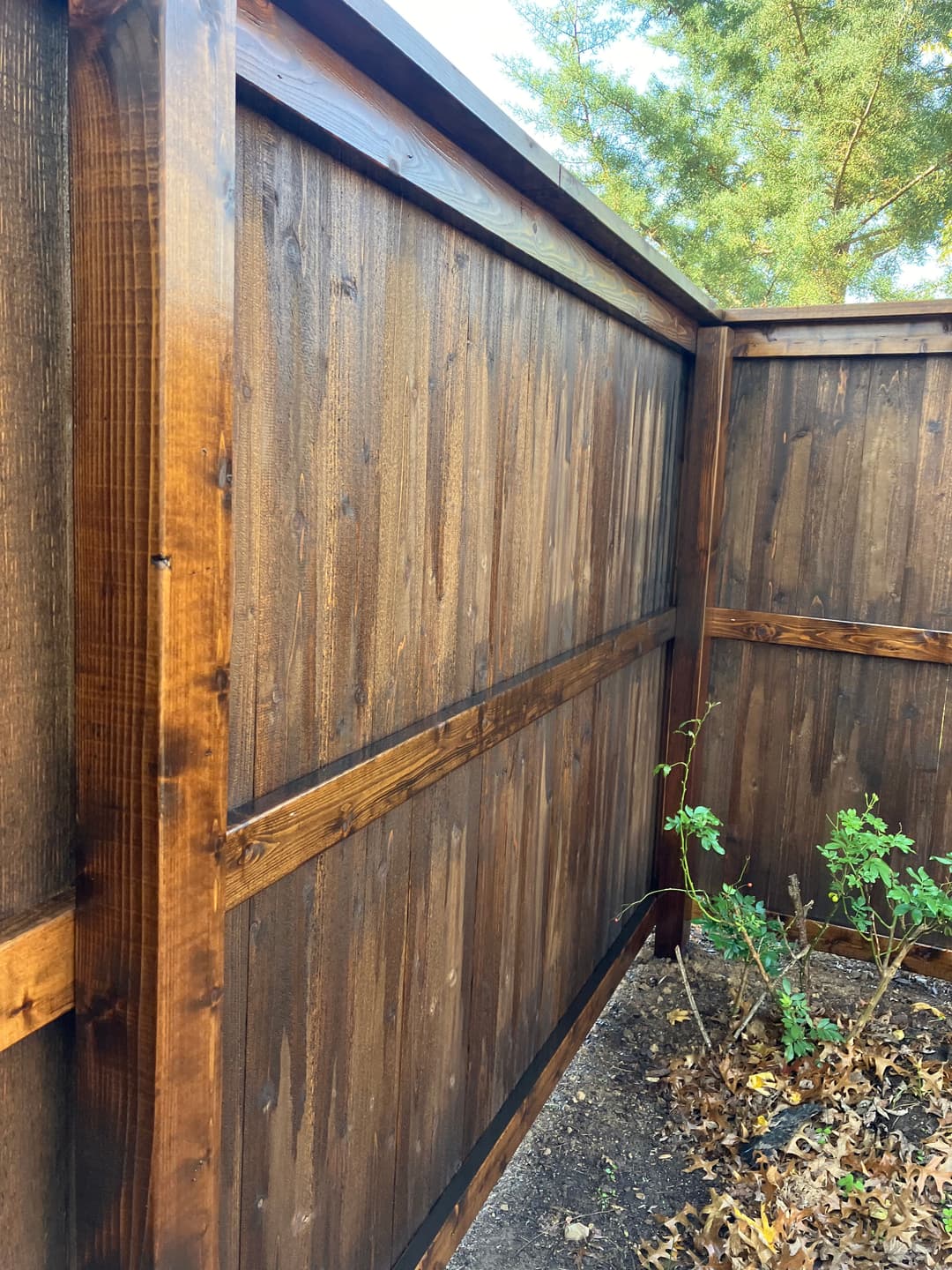 Wooden fence with rich brown finish and clean lines, surrounded by greenery and fallen leaves.