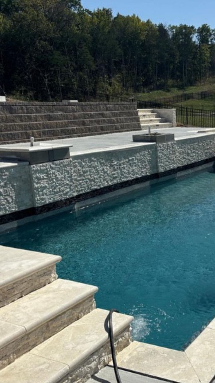 Modern pool with elegant stone steps and landscaped surroundings on a sunny day.