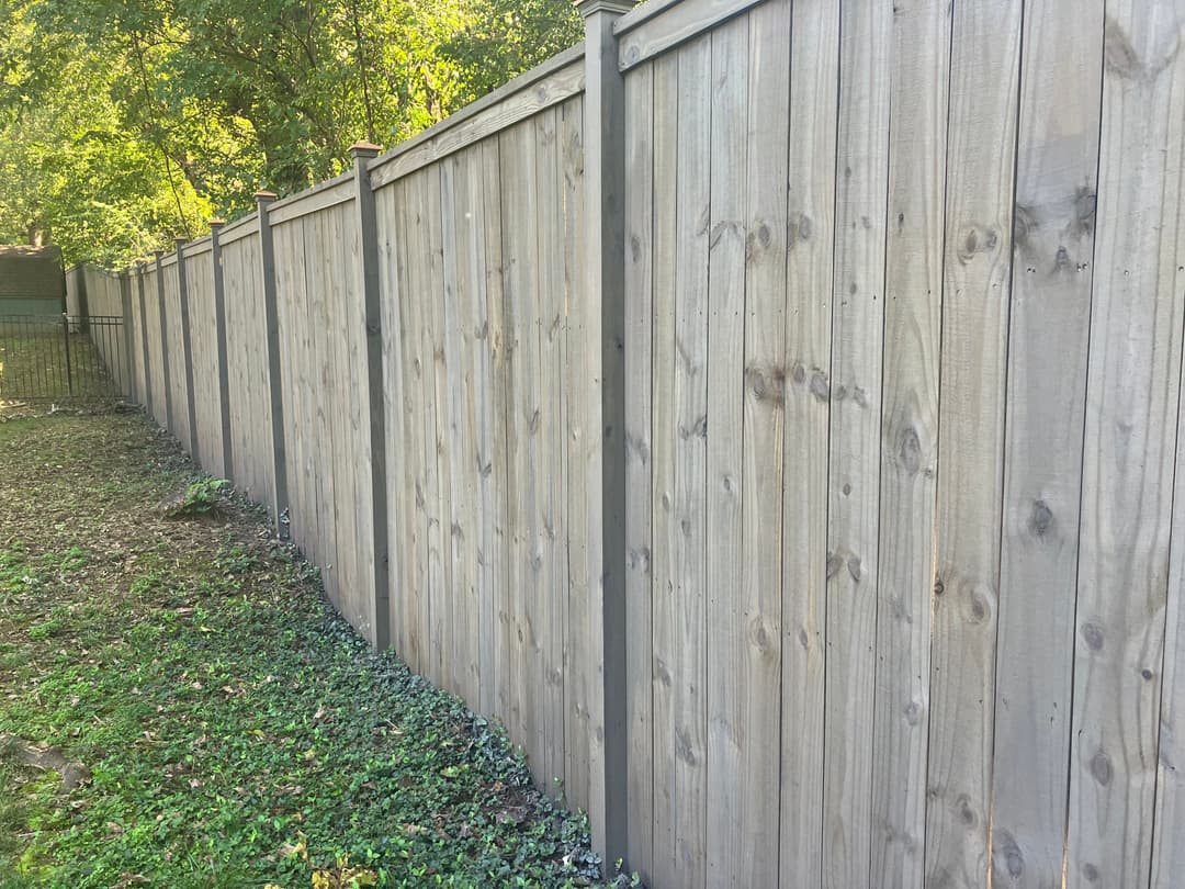 Wooden fence along a grassy yard, with metal posts and green foliage in the background.
