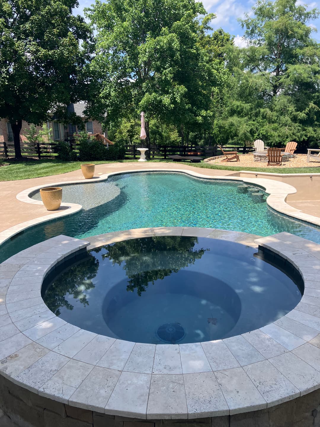 Elegant outdoor swimming pool with a spa, surrounded by lush greenery and a serene atmosphere.