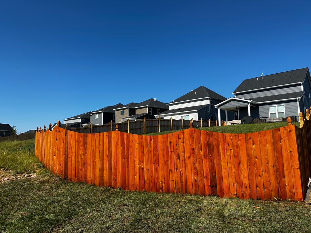Wooden fence with pointed tops separating backyards under a clear blue sky.