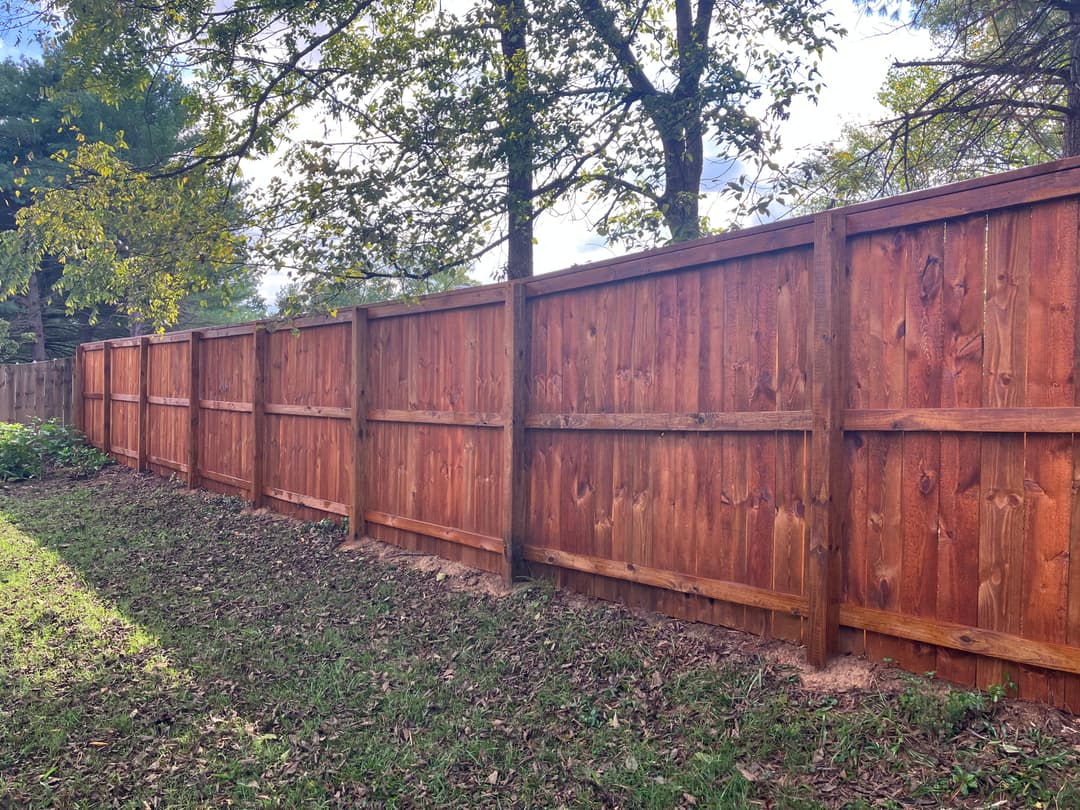 Wooden privacy fence lined with trees and grass under a sunny sky.