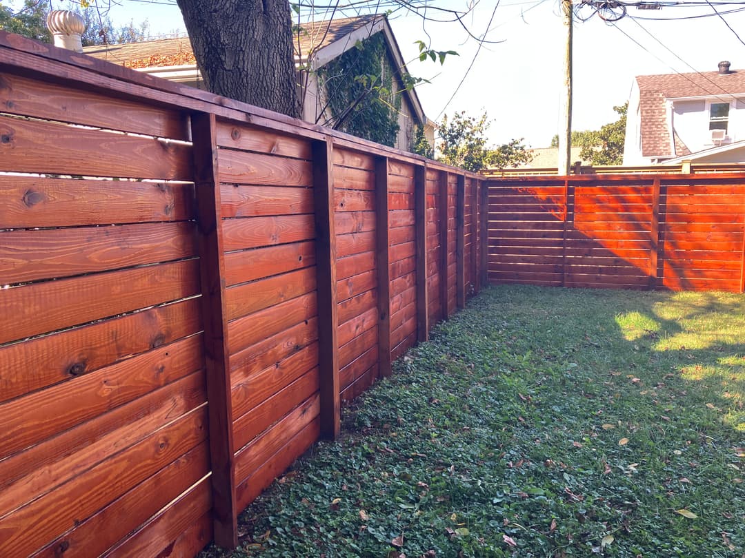 Wooden privacy fence in a sunny backyard with green grass and trees in the background.