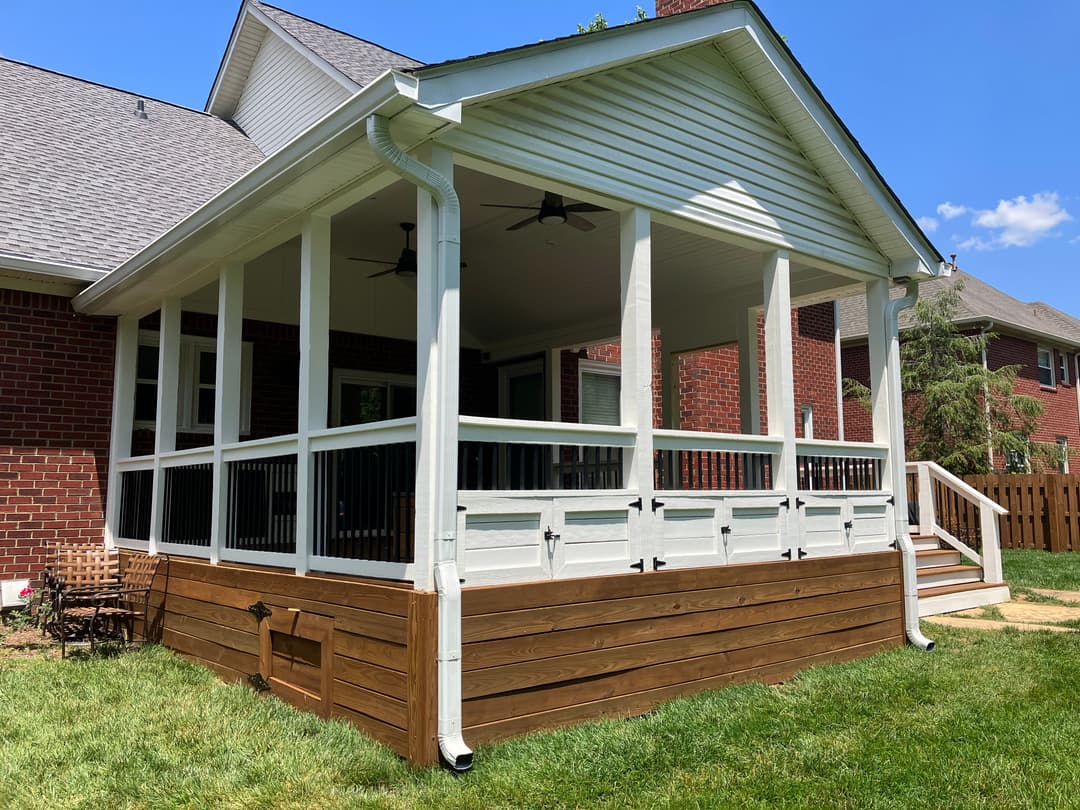 White screened porch with wooden accents and ceiling fans set in a sunny backyard.