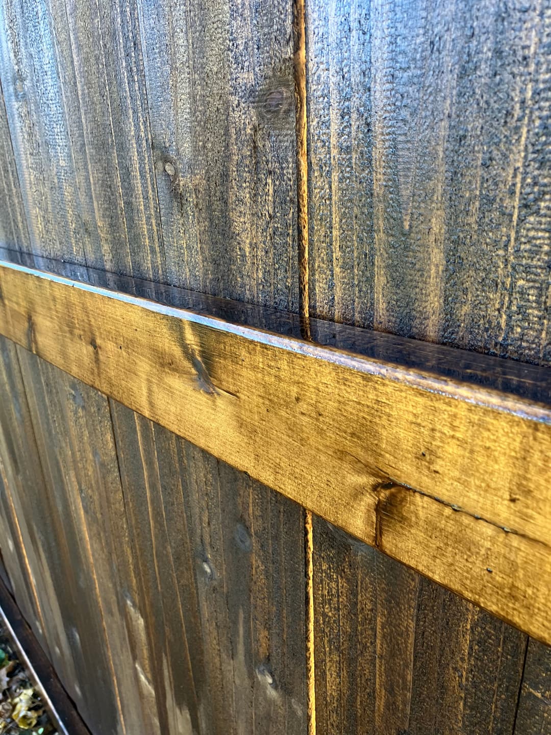 Close-up of a wooden fence with a dark finish and contrasting light wooden horizontal slat.