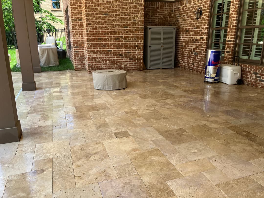 Patio with travertine stone flooring, brick walls, and outdoor storage containers.