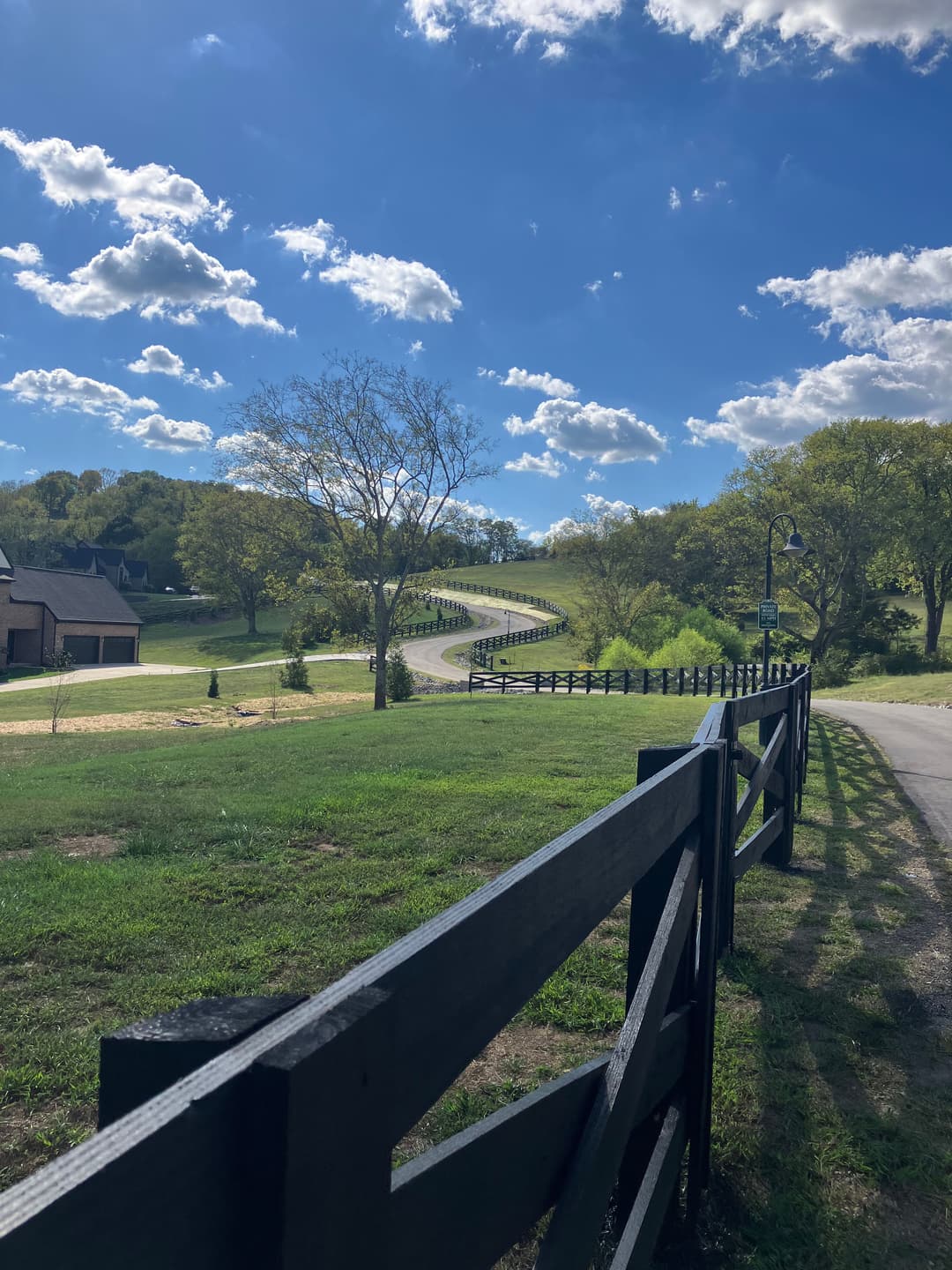 Scenic winding road lined with a black wooden fence under a bright blue sky.