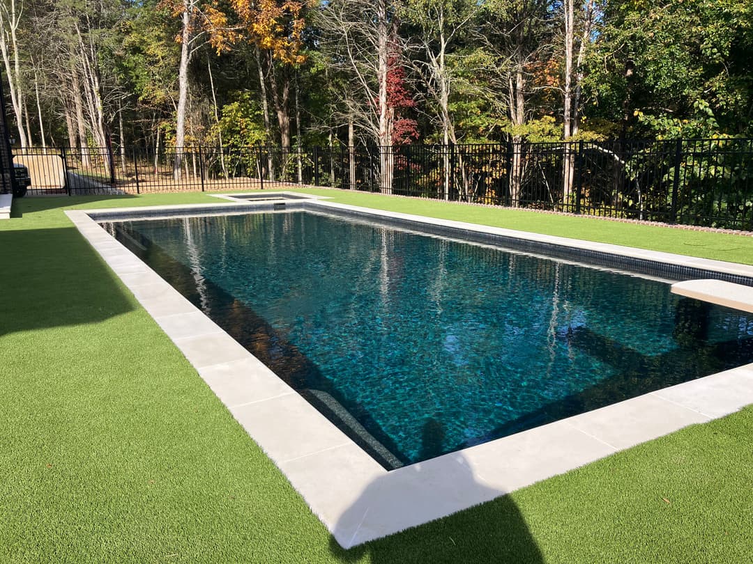 Modern inground swimming pool surrounded by lush greenery and a stylish fence.