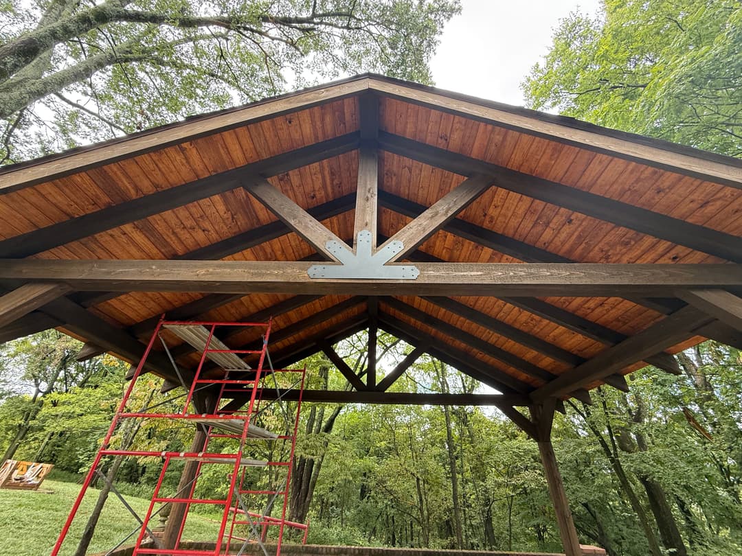 Wooden pavilion interior with rustic beams and scaffold for construction in a forested setting.