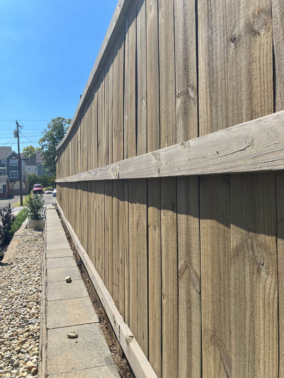 Wooden fence along a path with stones under clear blue sky on a sunny day.