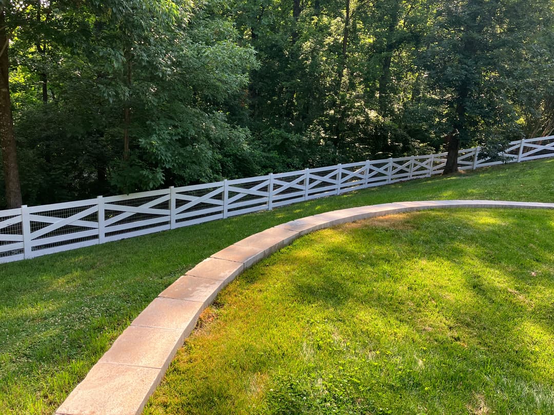 Curved stone pathway leading to a white wooden fence in a lush green landscape.